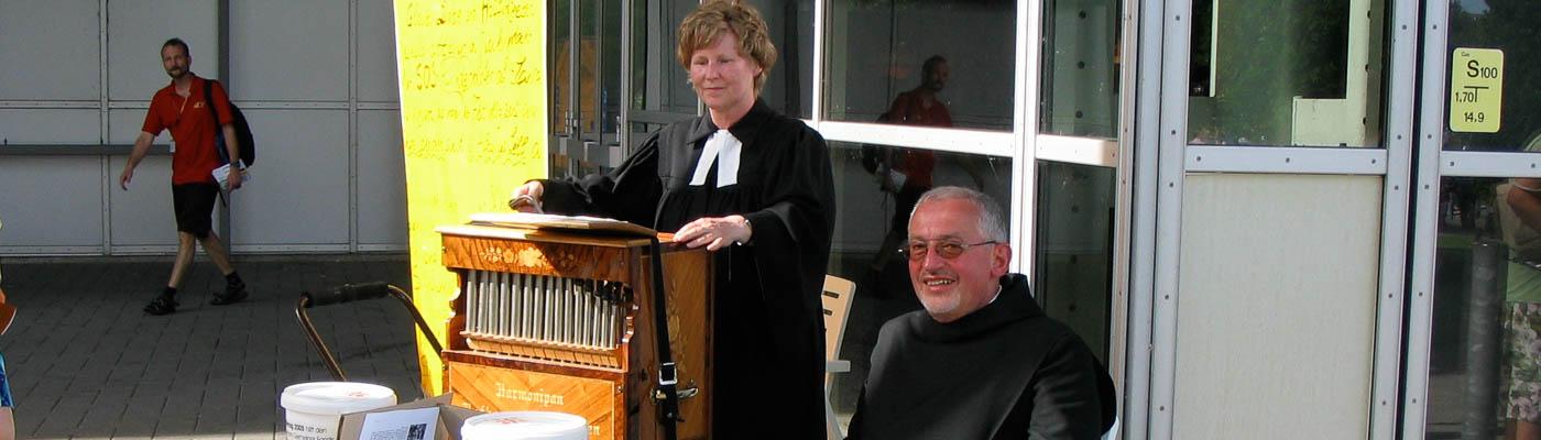 Pfarrerin und Mönch gemeinsam mit Leierkasten