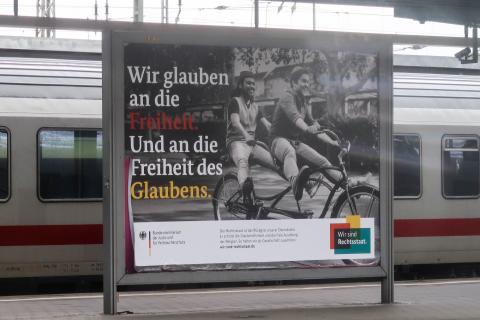 Plakat mit Muslim und Juden auf einem Tandem und Aufschrift: Wir glauben an die Freiheit. Und an die Freiheit des Glaubens. (Bundesjustizministerium)